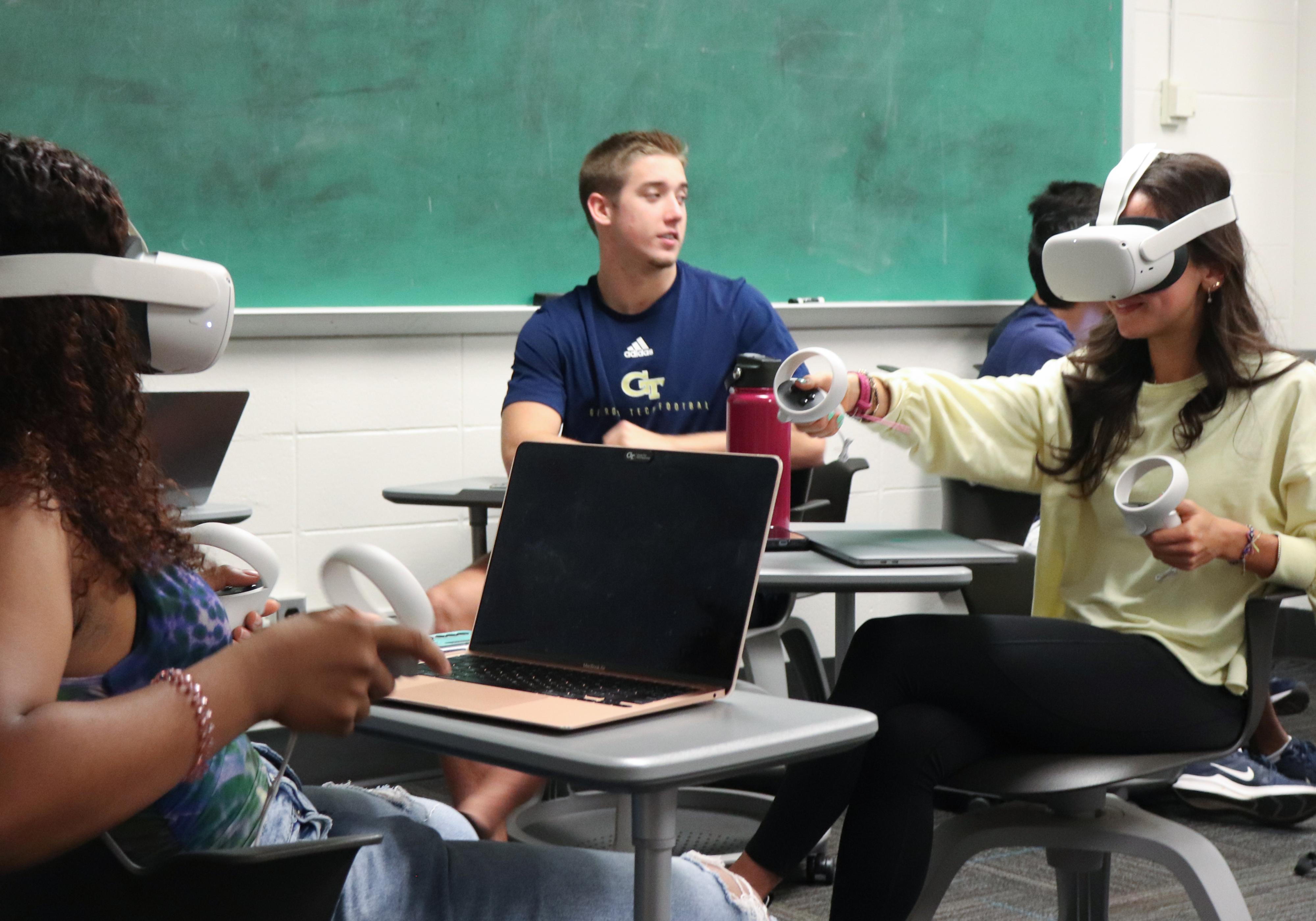 Two students wearing VR head-gear and another watching.